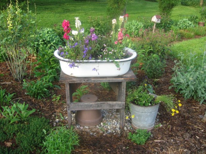 Old enamel pan on a wooden stand is centered in the garden bed